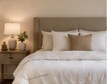Neutral bedroom with soft white bedding and warm bedside lighting