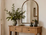 Wooden entryway console styled beneath an arched mirror
