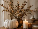 White pumpkin and glowing candles beside autumn branches